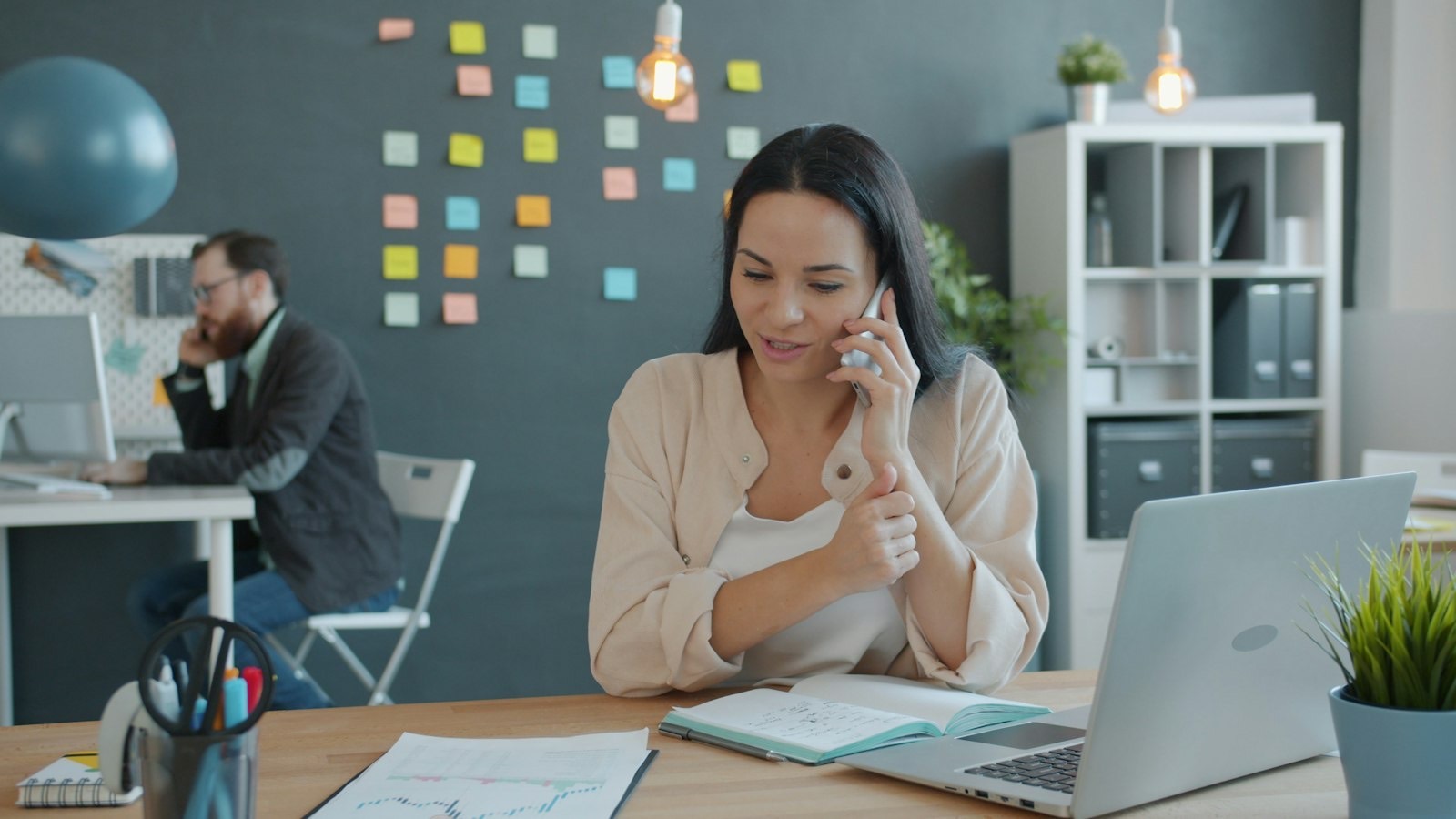 An office coordinator smiles while talking on the phone at her desk.