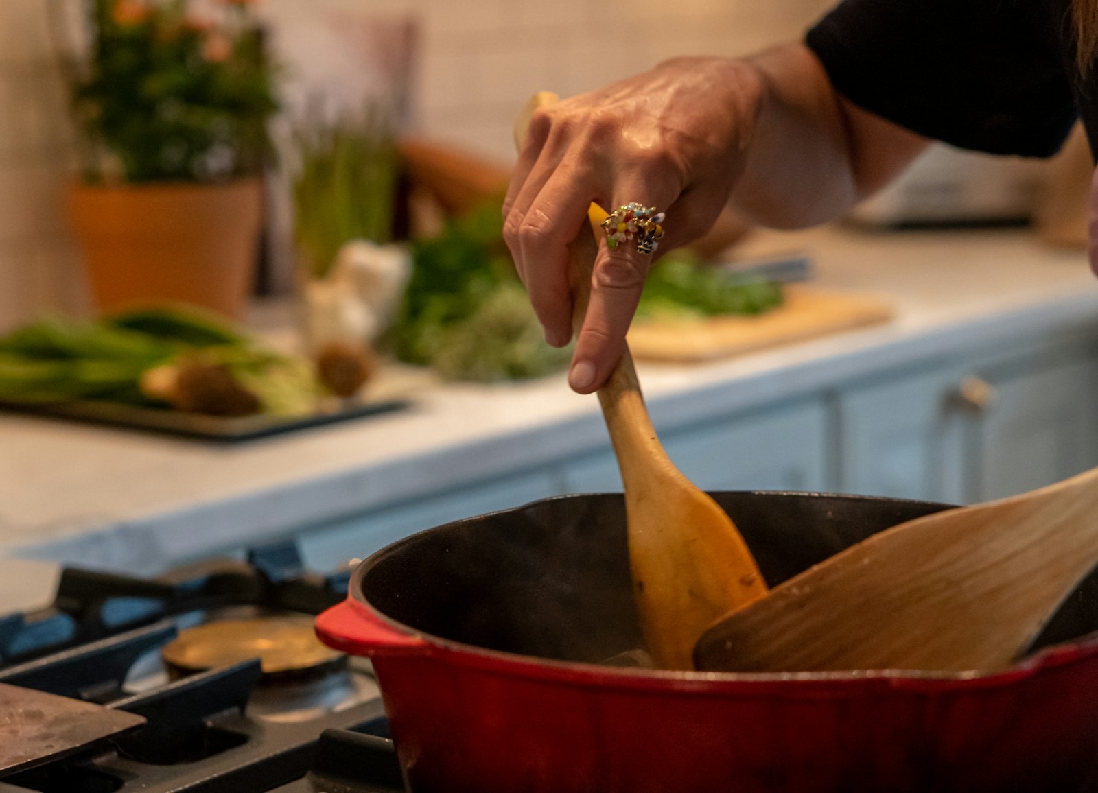 A hand stirring a red pot with a wooden spoon in a warm home kitchen.